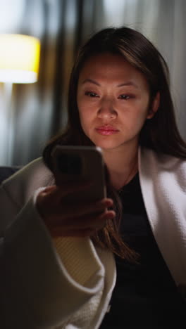 Vertical-Video-Of-Woman-Spending-Evening-At-Home-Sitting-On-Sofa-With-Mobile-Phone-Scrolling-Through-Internet-Or-Social-Media-1